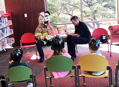 Firefighter and Person in Sparky the Dog Costume Reading to Kids